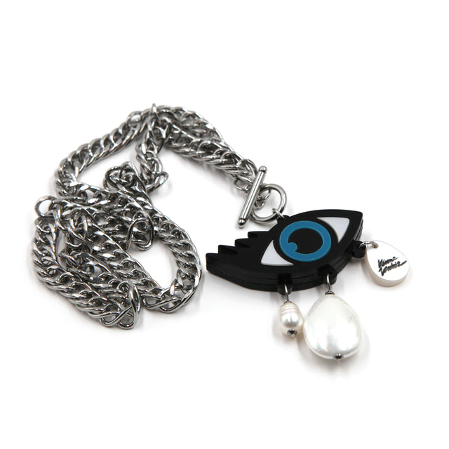 vue de côté d'un collier mauvais oeil en acrylique découpé au laser avec breloques perle d'eau douce, goutte en nacre montés sur une chaîne gourmette en acier inoxydable épaisse, sur fond blanc