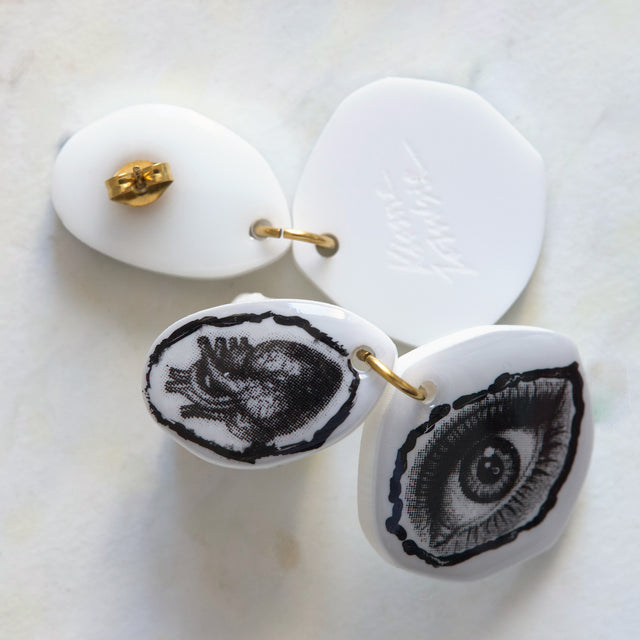 Gros plan sur les motifs cœur anatomique et œil des boucles d’oreilles DRAMARAMA en acrylique blanc