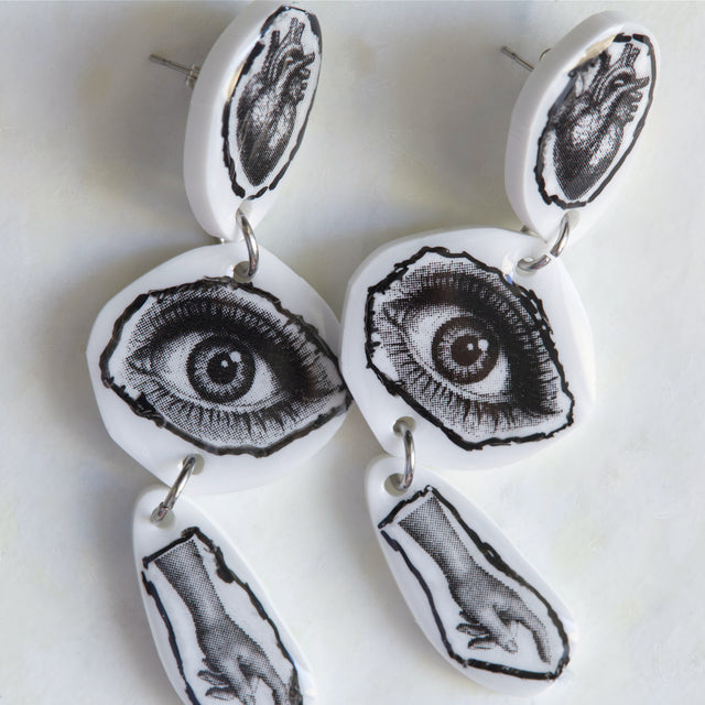 Détail des boucles d’oreilles DRAMARAMA avec cœur anatomique, œil et main en noir et blanc