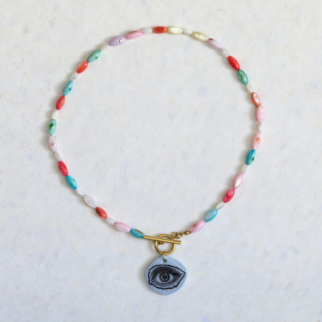 Collier DRAMARAMA en nacre colorée et blanche avec pendentif œil bleu et fermoir doré
