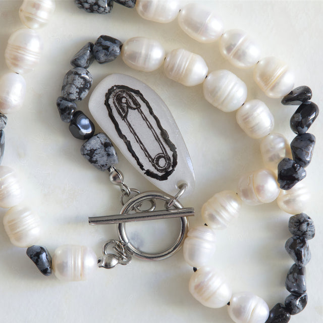 Gros plan sur le pendentif épingle, les perles d’eau douce et les nuggets d’obsidienne du collier DRAMARAMA