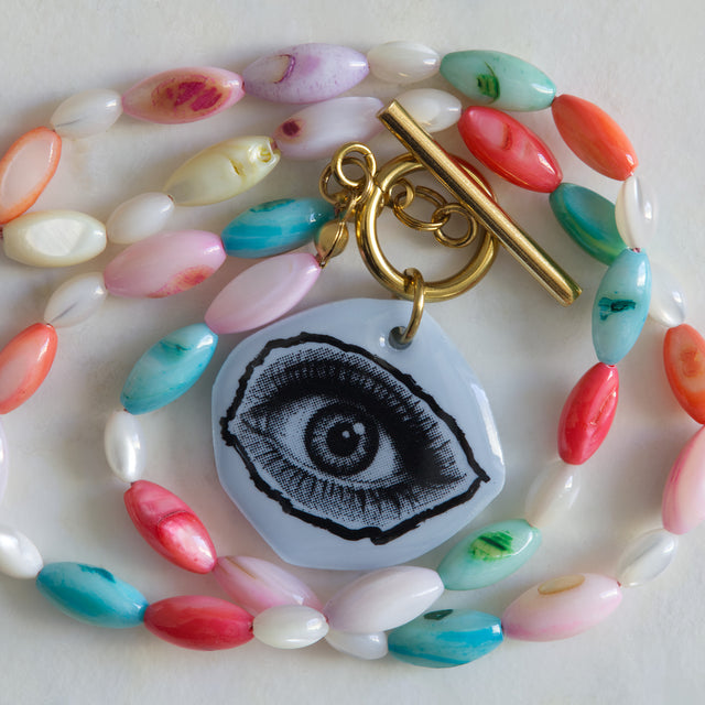 Gros plan sur le pendentif œil en acrylique bleu et les perles de nacre colorée du collier DRAMARAMA