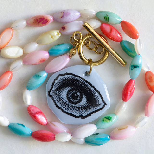 Gros plan sur le pendentif œil en acrylique bleu et les perles de nacre colorée du collier DRAMARAMA