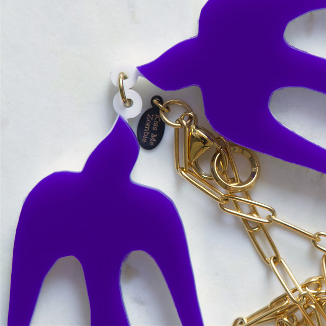 Gros plan sur les hirondelles violettes, la chaîne dorée et le fermoir du collier Henri