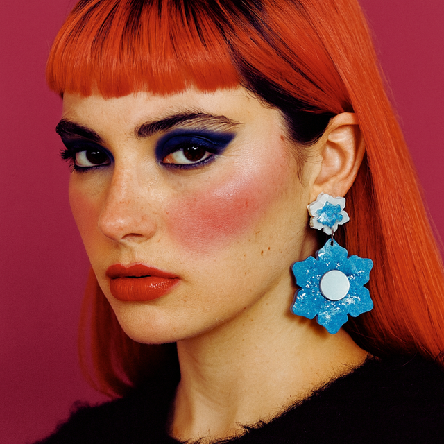 femme de trois quart sur fond rose fuchsia portant les boucles d'oreilles statement en résine et plexi