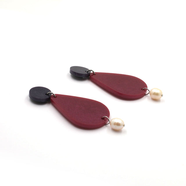 picture of earrings on a white background. the earrings are composed by a purple dot at the top, then a bigger dark pink pear shape and a freshwater pearls at the bottom hanging.