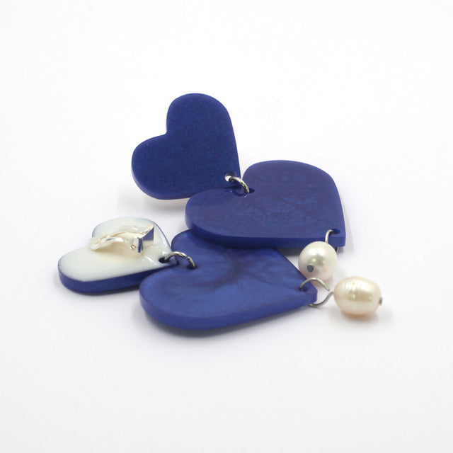This is a picture of blue hearts earrings with freshwater pearls on a white background. one is on the back, the clip on are silver with silicone pad protection.