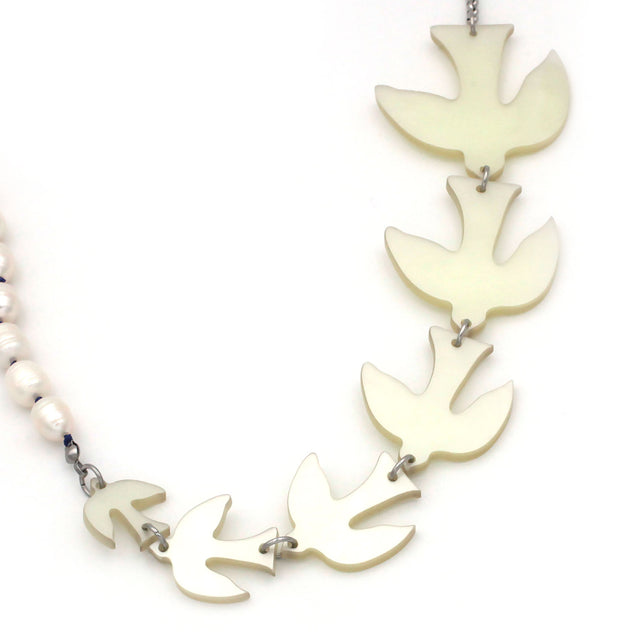 A close up picture of white birds of different sizes and pearls on a sautoir long necklace on a white background. 