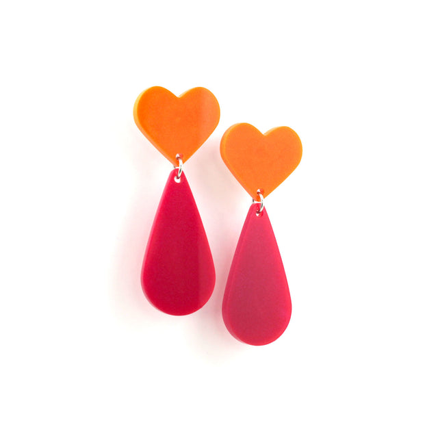 This is a picture of dangles earrings on a white background. The top of the earrings are orange heart and the pendants are pink teardrop.