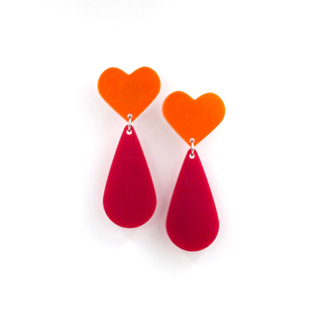 This is a picture of dangles earrings on a white background. The top of the earrings are orange heart and the pendants are pink teardrop.
