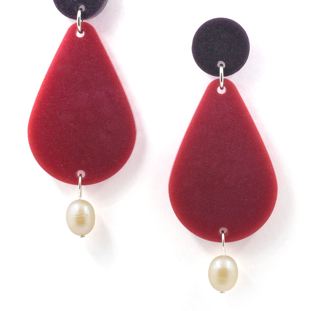 picture of earrings on a white background. the earrings are composed by a purple dot at the top, then a bigger dark pink pear shape and a freshwater pearls at the bottom hanging.