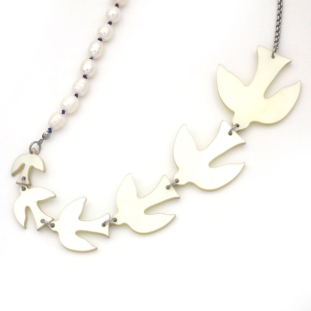 A close up picture of white birds of different sizes and pearls on a sautoir long necklace on a white background.