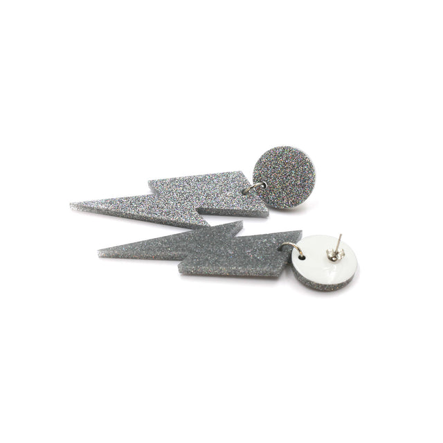this is a picture of silver holographic glitter bolt and dot dangle earrings on a white background. one is on the back, the stud are silver on a white dot.