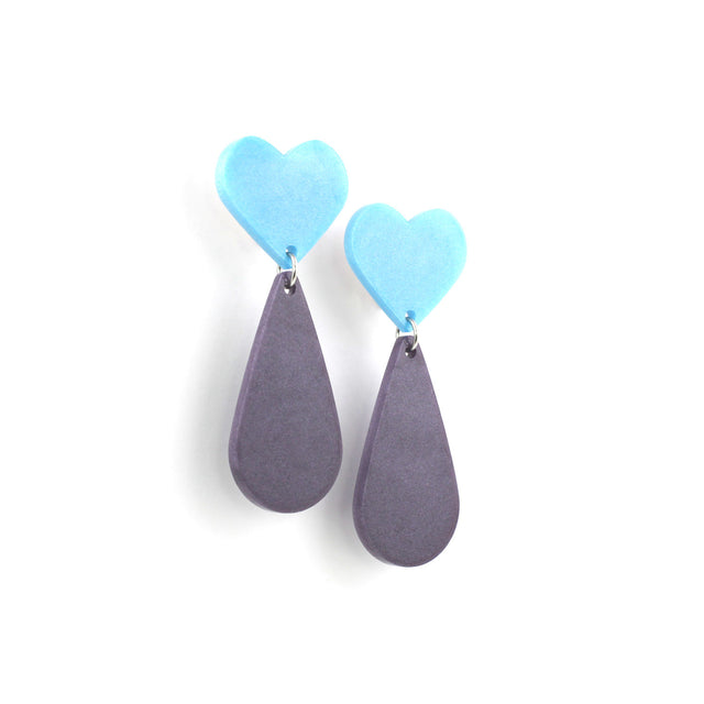 This is a picture of dangles earrings on a white background. The top of the earrings are blue heart and the pendants are purple teardrop. 