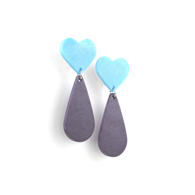 This is a picture of dangles earrings on a white background. The top of the earrings are blue heart and the pendants are purple teardrop.