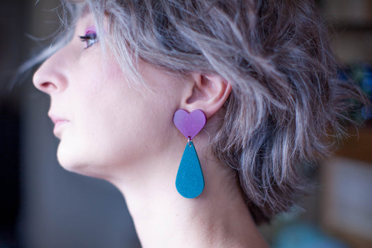this is a picture of a dark blond woman profile. she's wearing heart and teardrop earrings. she has short hair. the background is blurry