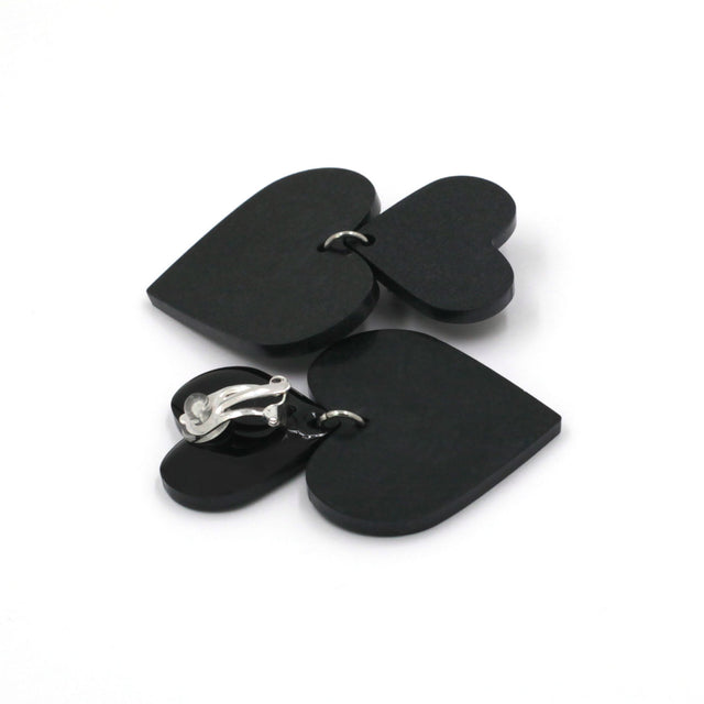 black hearts earrings on a white background. one is on its back, there is a clip on earring with a silicone pad protection. 
