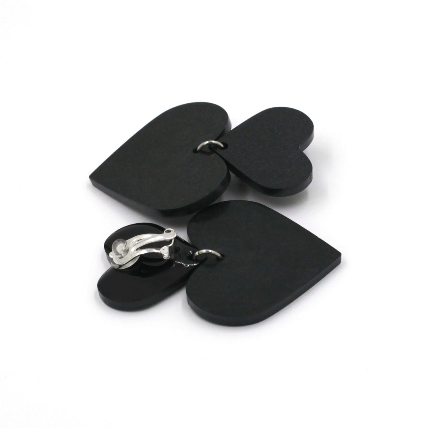 black hearts earrings on a white background. one is on its back, there is a clip on earring with a silicone pad protection. 