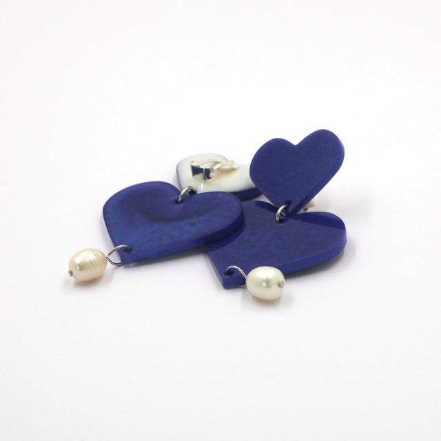 This is a picture of blue hearts earrings with freshwater pearls on a white background.  one is on the back, the clip on are silver with silicone pad protection. 