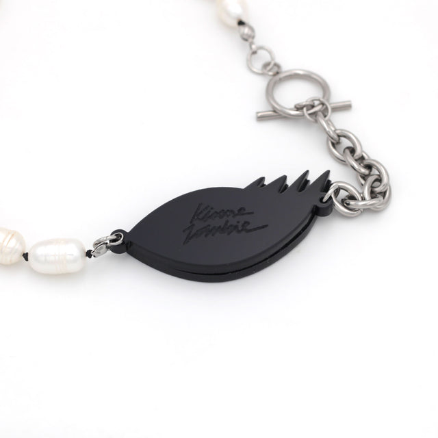 Close-up of a laser-cut engraved logo, kiss me zombie, on the back of an evil eye and freshwater pearls necklace on a white background.