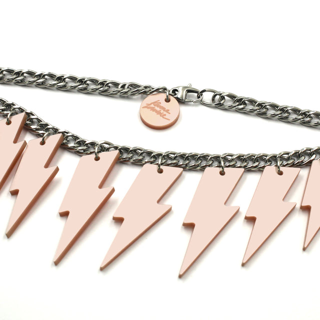 This is close up photo of a necklace composed of a chunky silver tone curb chain pink pearly lightning bolts of graduant size on a white background. on the lobster clasp there is a round charm with the kissmezombie logo engraved on it.