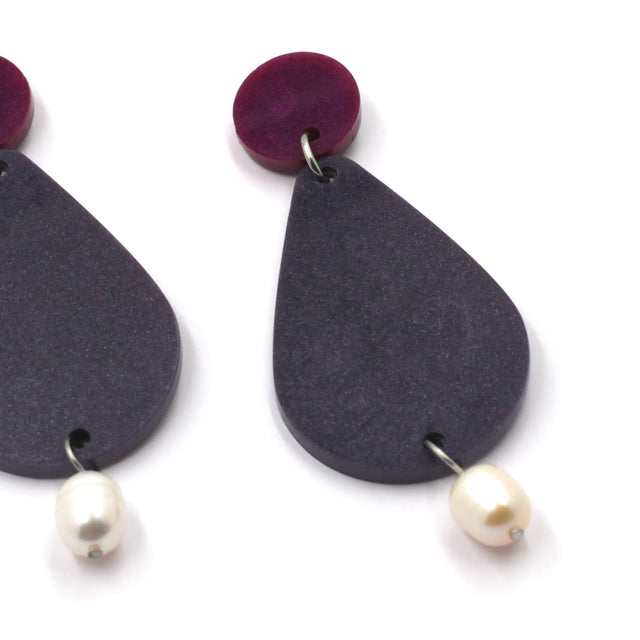 close up picture of earrings on a white background. the earrings are composed by a pink dot at the top, then a bigger purple pear shape and a freshwater pearls at the bottom hanging.