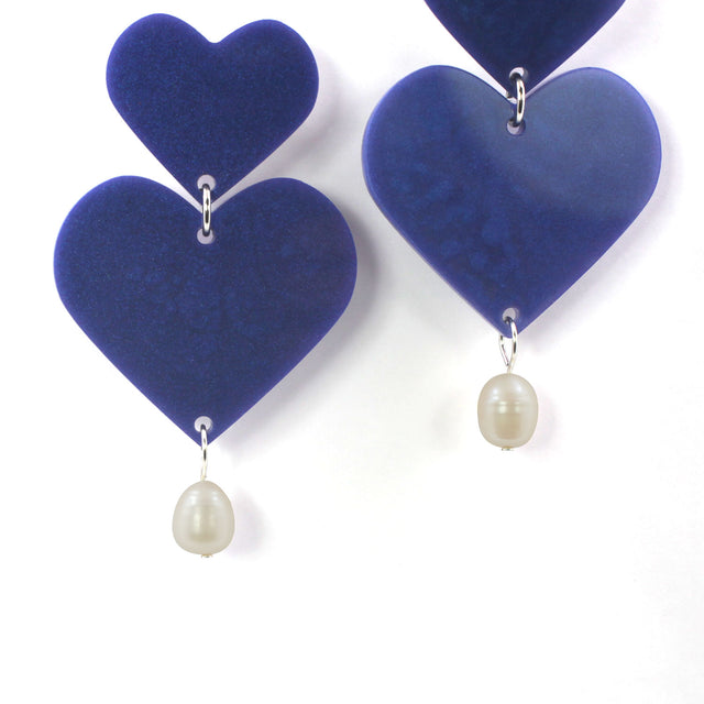 This is a close up picture of purple hearts earrings with freshwater pearls on a white background.