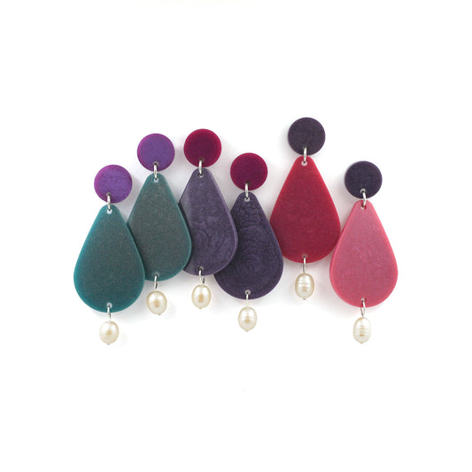 picture of three pairs of earrings hanging from a white background. They are the same design, a small dot at the top of the earrings and a bigger size pear dangles and freshwater pearls. Three different colors, one is purple and green, one in the middle are purple and pink and the right one are, pink and purple with freshwater pearls. 