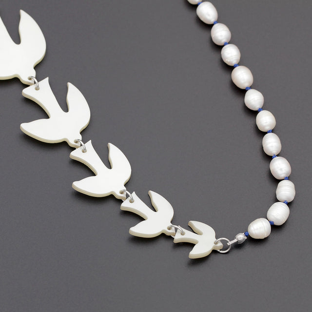 A close up picture of white birds of different sizes and pearls on a sautoir long necklace on a black background. 