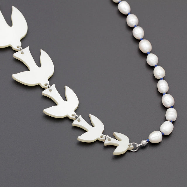 A close up picture of white birds of different sizes and pearls on a sautoir long necklace on a black background.