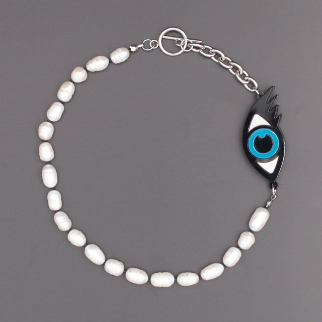Playful laser cut blue evil eye with freshwater pearls, a chunky chain, and a toggle clasp on a black background.