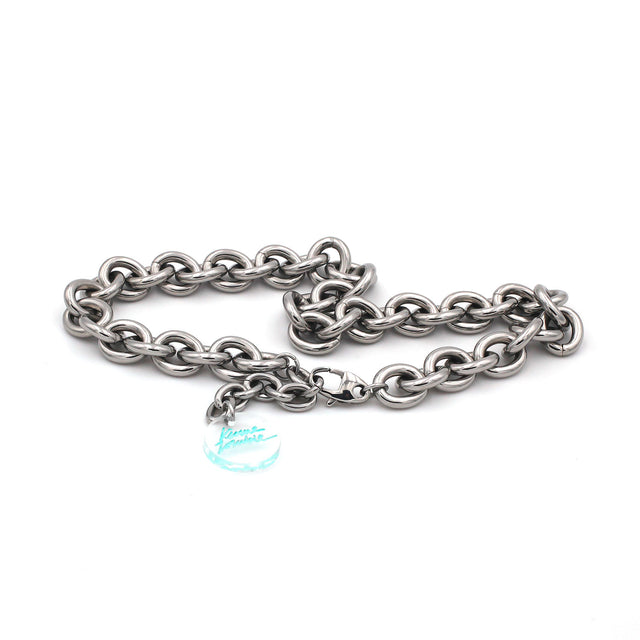 this is a picture of a massive link cable stainless steel chain choker necklace hanging from a white background. there is an extender with a clear engraved medal with green signature logo.