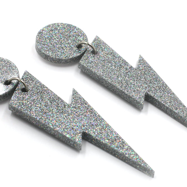 this is a close up picture of silver holographic glitter bolt and dot dangle earrings on a white background.