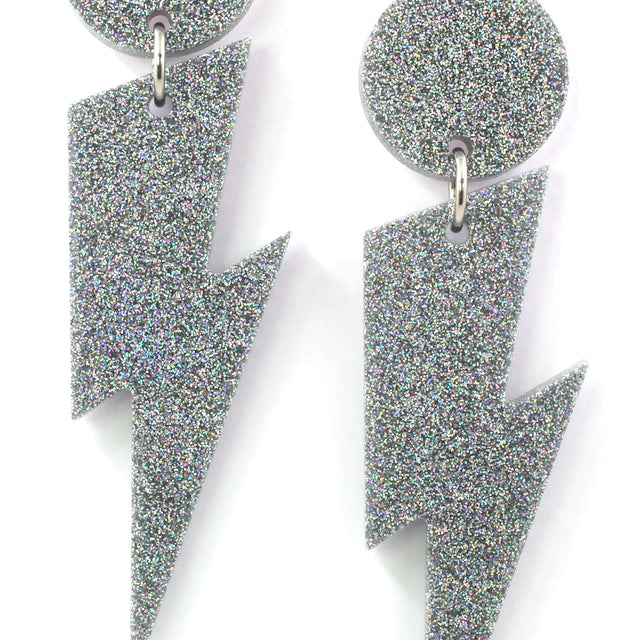 this is a close up picture of silver holographic glitter bolt and dot dangle earrings on a white background.