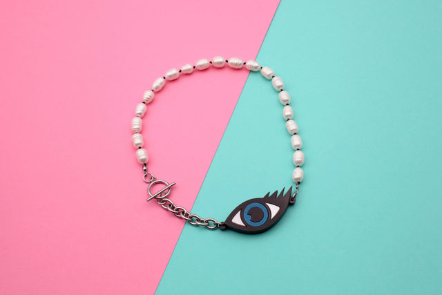 statement, evil eye and pearls necklace, on a pink and blue background.