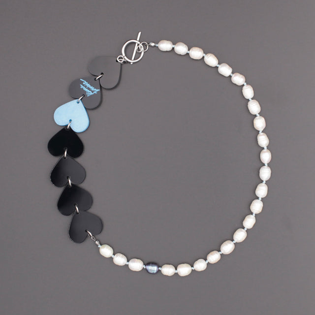 Laser-cut and resin black and blue hearts necklace with freshwater pearls and toggle clasp on a black background.