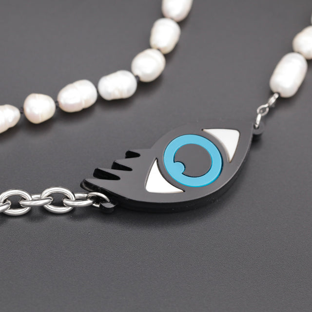 Close-up of a playful laser-cut blue evil eye with freshwater pearls, on a black background.