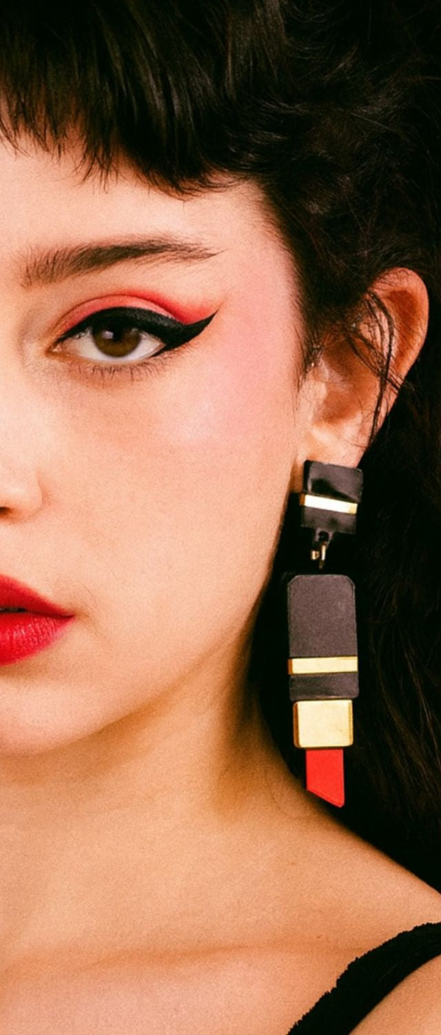Portrait rapproché d’une femme au maquillage graphique avec des boucles d’oreilles en forme de rouge à lèvres, en acrylique découpé laser, bijou statement fait main à Marseille par Kiss Me Zombie.