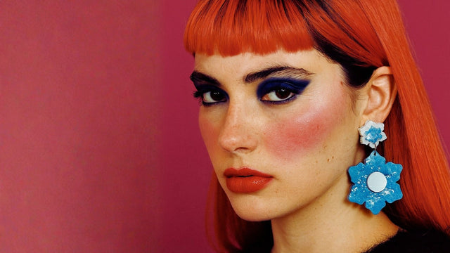 Femme au regard intense portant une boucle d’oreille statement en forme de fleur bleue en résine. Bijou fait main à Marseille par Kiss Me Zombie, marque rebelle et poétique.