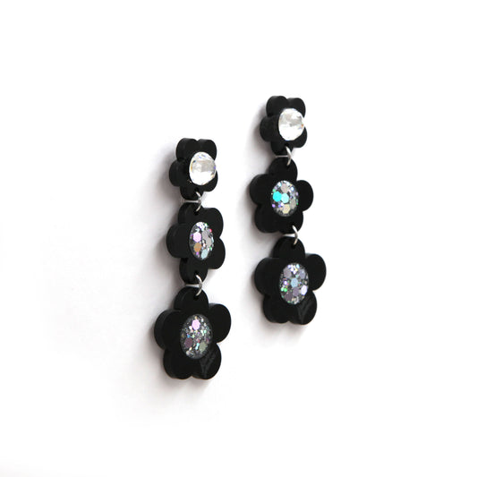 side view of Black laser cut acrylic flowers earrings with glitter center on a white background