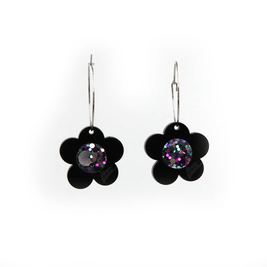 black laser cut acrylic flower with a pink glittery resin center hoop earrings on a white background