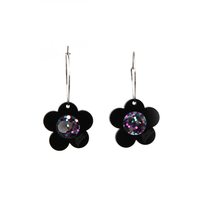 close up of black laser cut acrylic flower with a pink glittery resin center hoop earrings on a white background
