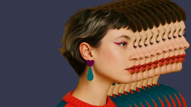 Portrait de profil d’une femme portant une boucle d’oreille statement cœur violet et goutte vert canard, sur fond violet avec effet de duplication pop. Bijou fait main à Marseille par Kiss Me Zombie.