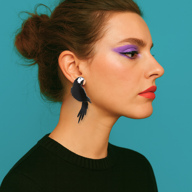Portrait studio d’une femme portant des boucles d’oreilles perroquet noir Kiss Me Zombie, en acrylique découpé au laser, peintes et assemblées à la main. Bijoux statement au style arty et punk-chic, fond turquoise, lumière douce mettant en valeur les détails.
