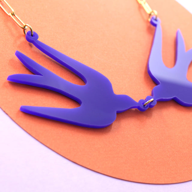 Vue de côté du collier plastron oiseaux bleu Klein, mettant en valeur son design sculptural et sa chaîne graphique.