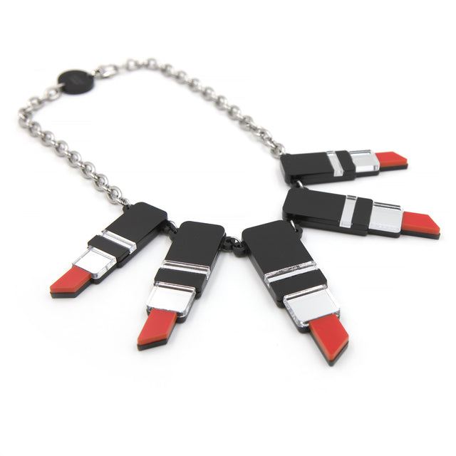 vu de côté du un collier plastron tube de rouge à levre en acrylique découpé au laser, noir, rouge et miroir argenté avec une grosse chaine forçat en acier inoxydable sur fond blanc