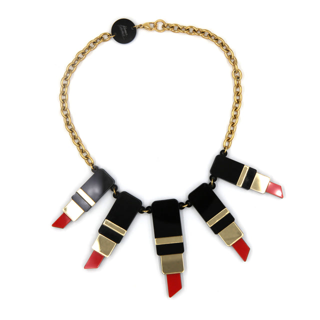 vu du dessus d'un collier plastron composé de tube de rouge à lèvre en acrylique noir, rouge et miroir doré avec une grosse chaîne en acier doré à l'or fin sur fond blanc