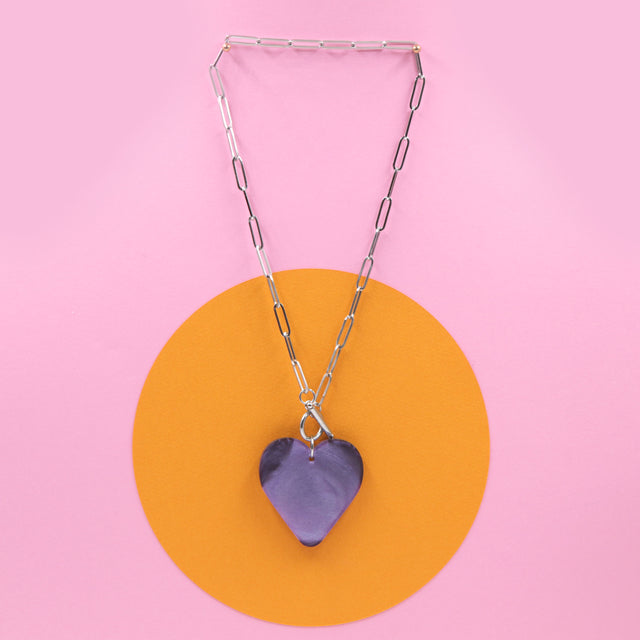 vu en entier du collier cœur violet marbré – bijou audacieux et original pour un style unique sur un fond en papier coloré.