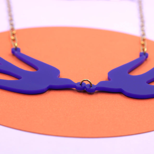 Zoom sur le collier oiseaux bleu Klein, acrylique découpé au laser, avec une chaîne en acier inoxydable doré à l’or fin.