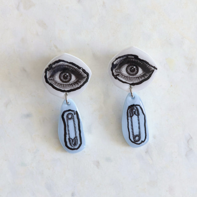 Boucles d’oreilles DRAMARAMA avec œil noir et blanc et épingle à nourrice sur acrylique bleu pâle